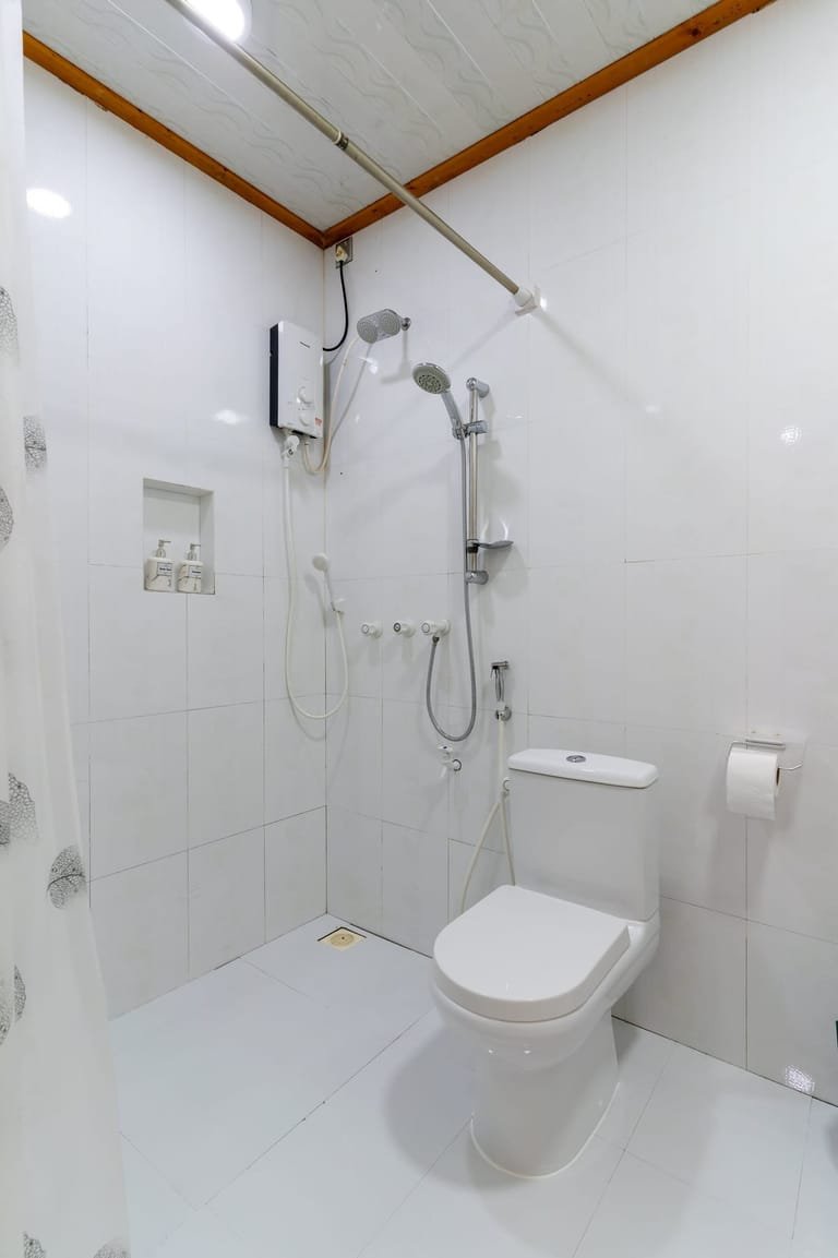 Shower and electric water heater in the white bathroom at Maafolhey Han'dhaan.