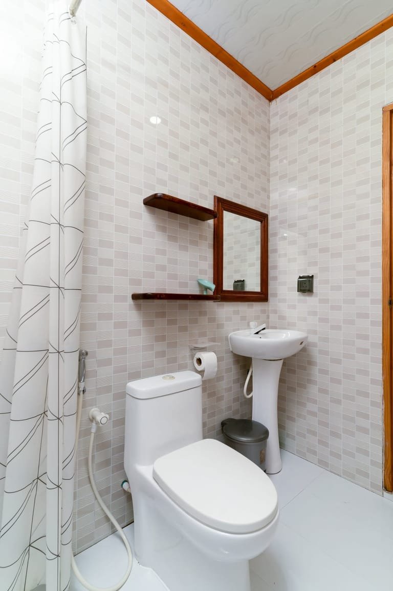 White-tiled bathroom at Maafolhey Han'dhaan with shower, toilet, and sink.